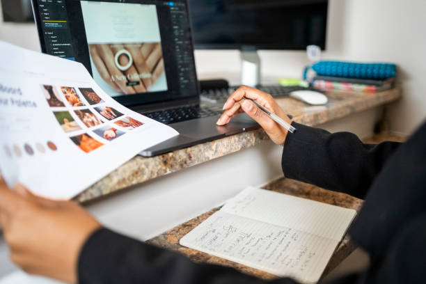 Cropped shot of a female website developer holding product portfolio while designing a webpage on laptop at creative office